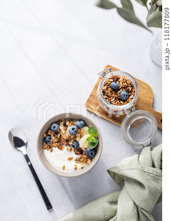 Muesli with vegetarian yogurt, banana and blueberries in a bowl on a light background. Muesli with vegetarian yogurt, banana and blueberries in a bowl on a light background. 118177809