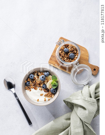 Muesli with vegetarian yogurt, banana and blueberries in a bowl on a light background. Muesli with vegetarian yogurt, banana and blueberries in a bowl on a light background. 118177813