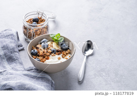 Muesli with vegetarian yogurt, banana and blueberries in a bowl on a light background.  118177819