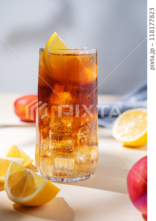 Iced tea with lemon, peach and ice in a tall glass on a yellow background with shadow and fruits. Iced tea with lemon, peach and ice in a tall glass on a yellow background with shadow and fruits. 118177823