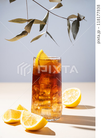 Iced tea with lemon and ice in a tall glass on a yellow and blue background with shadow and branch. Iced tea with lemon and ice in a tall glass on a yellow and blue background with shadow and branch. 118177838