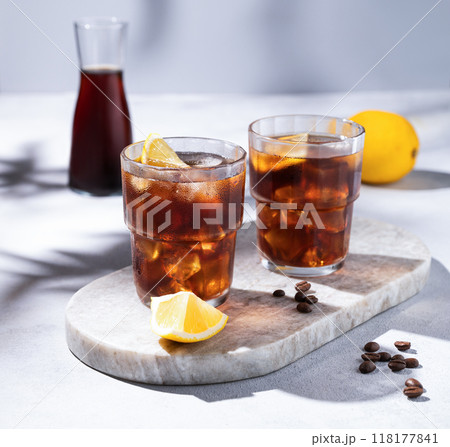 Cold brew coffee in a two glasses with lemon and ice on a marble board on a light background  118177841
