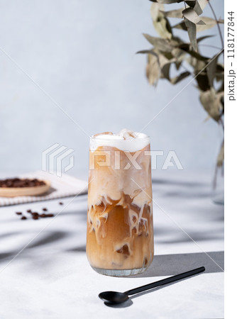 Iced coffee latte in a tall glass with milk on a light background with coffee beans, spoon 118177844