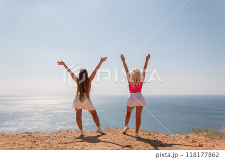 Two women are standing on a hill overlooking the ocean 118177862