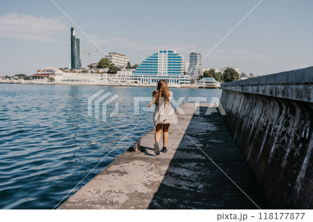 woman in a white dress is walking on a pier near the water. The scene is peaceful and serene, with the woman's long hair blowing in the wind. 118177877