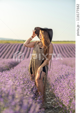 A woman is standing in a field of purple flowers, wearing a black dress and a black hat. A woman is standing in a field of purple flowers, wearing a black dress and a black hat. 118177882