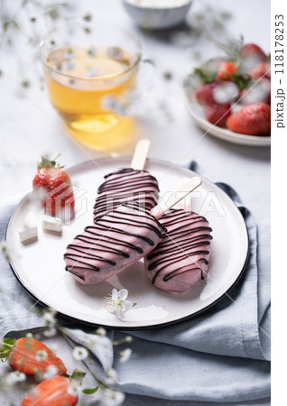Chocolate cake pops ice cream on a stick in pink glaze on a plate with berries on a light background Chocolate cake pops ice cream on a stick in pink glaze on a plate with berries on a light background 118178253