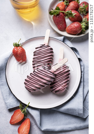 Chocolate cake pops ice cream on a stick in pink glaze on a plate with berries on a light background Chocolate cake pops ice cream on a stick in pink glaze on a plate with berries on a light background 118178257
