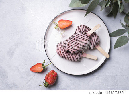Chocolate cake pops ice cream on a stick in pink glaze on a plate with berries and eucaluptus  118178264
