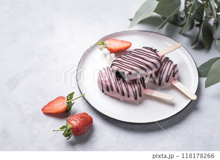 Chocolate cake pops ice cream on a stick in pink glaze on a plate with berries and eucaluptus  Chocolate cake pops ice cream on a stick in pink glaze on a plate with berries and eucaluptus  118178266