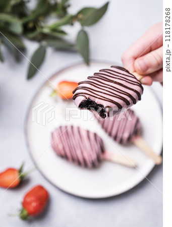 Chocolate cake pops ice cream on a stick in pink glaze bitten off is hold by a child's hand  118178268