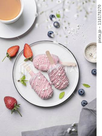Chocolate cake pops ice cream on a stick in pink glaze on a plate with berries on a light background 118178270