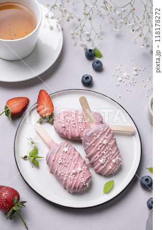 Cake pops ice cream on a stick in pink glaze on a plate with berries on a light background Cake pops ice cream on a stick in pink glaze on a plate with berries on a light background 118178272