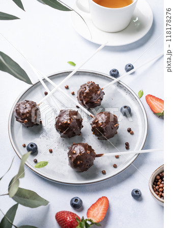 Chocolate cake pops with nuts on a plate with fresh berries and cup of tea on a light background.  118178276
