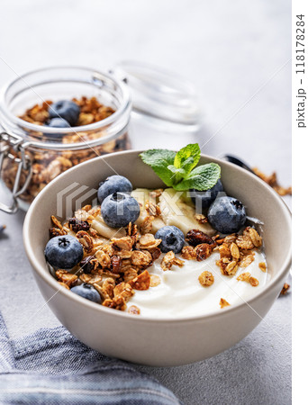 Muesli with vegetarian yogurt, banana and blueberries in a bowl on a light background close up.  118178284