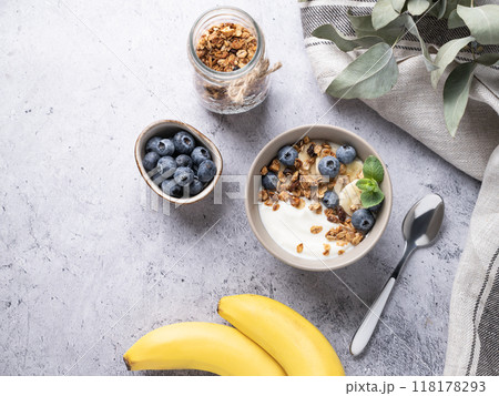 Muesli with vegetarian yogurt, banana and blueberries in a bowl on a gray texture background. Muesli with vegetarian yogurt, banana and blueberries in a bowl on a gray texture background. 118178293