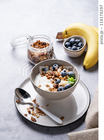 Muesli with vegetarian yogurt, banana and blueberries in a bowl on a gray texture background. Muesli with vegetarian yogurt, banana and blueberries in a bowl on a gray texture background. 118178297
