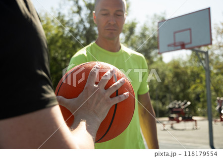 Two basketball players holding orange ball on sports court. Sports goals competition game, champion outdoor workout. Close up. Game moment. Two basketball players holding orange ball on sports court. Sports goals competition game, champion outdoor workout. Close up. Game moment. 118179554