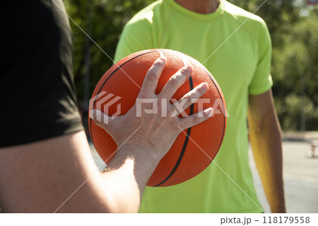 Hands of two basketball players holding orange ball on sports court. Sports goals competition game, champion outdoor workout. Close up. Game moment. 118179558