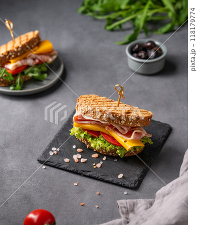 Club sandwich on a board with a bacon, cheese, tomato and lettuce on a dark background Club sandwich on a board with a bacon, cheese, tomato and lettuce on a dark background 118179774