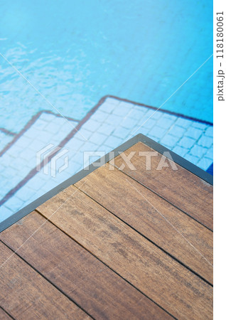 Empty wooden tabletop in front of a swimming pool with blue tile stairs.  118180061