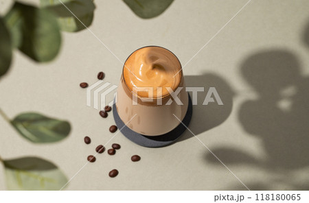 Dalgona coffee. Whipped instant coffee in a glass  with beans and shadow leaves on green background. 118180065