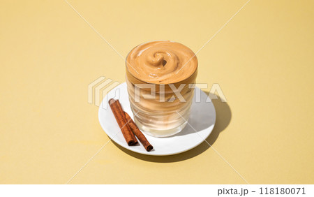 Dalgona coffee. Whipped instant iced coffee in a glass with cinnamon sticks on yellow background. 118180071