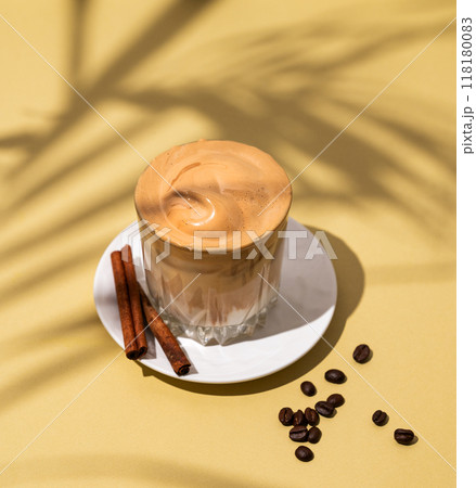 Dalgona coffee. Whipped instant coffee in a glass on a saucer with cinnamon sticks 118180083