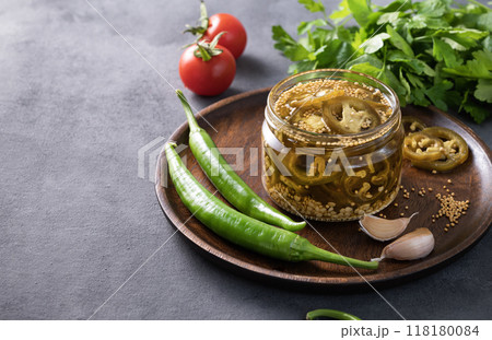 Jalapeno hot pepper, sliced in a jar with spices on a wooden plate with fresh vegetables  118180084