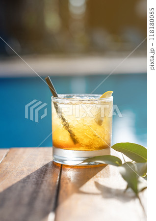 Alcohol cocktail with lemon on a wooden tabletop in front of the pool close-up.  118180085