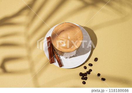 Dalgona coffee. Whipped instant coffee in a glass on a saucer with cinnamon sticks 118180086