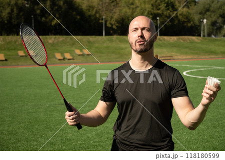 Man with badminton racket and white shuttlecock with emotions on green floor sport court in public park. Summer outdoor game. Badminton coach. Close up. 118180599