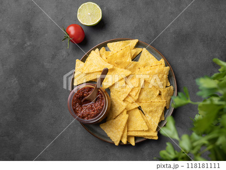 Nachos or tortilla with spicy tomato sauce on a plate  with fresh herbs on a dark background.  118181111