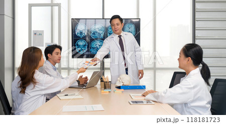 Group of doctor discussing brain scans on large monitor in a meeting room. A female doctor hand over meeting document to a doctor in white gown. Group of doctor discussing brain scans on large monitor in a meeting room. A female doctor hand over meeting document to a doctor in white gown. 118181723
