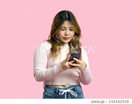 Young asian woman in casual clothing, holding and looking at a smartphone. Portrait on a simple pink background with studio light. Isolated Young asian woman in casual clothing, holding and looking at a smartphone. Portrait on a simple pink background with studio light. Isolated 118182529