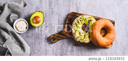 Bagel burger with ricotta, avocado and sesame seeds on a board top view web banner 118183652