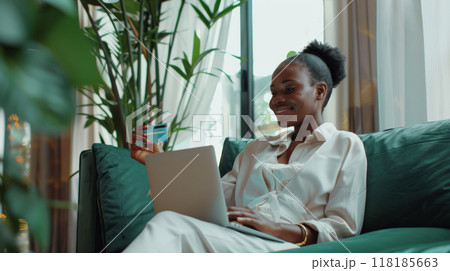 African American woman sitting background modern interior holding credit card her hand, web laptop 118185663