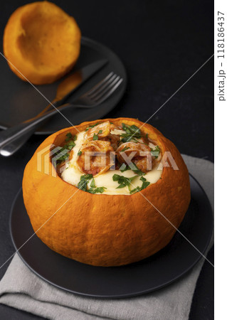 Whole baked pumpkin with tiger prawns, melted cheese and tomatoes. Traditional dish of Brazil, home cooking. Selective focus, close-up, black background. 118186437