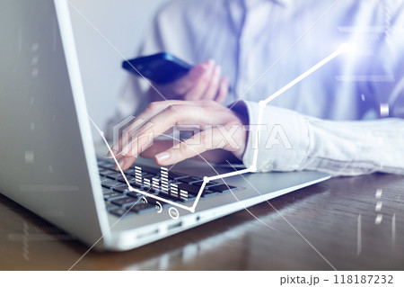 A person is typing on a laptop with a cell phone in their hand A person is typing on a laptop with a cell phone in their hand 118187232