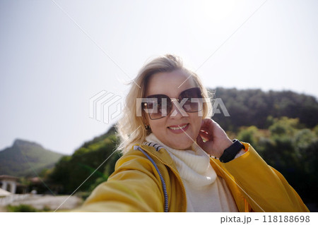 A woman wearing a yellow jacket and sunglasses is smiling for the camera 118188698