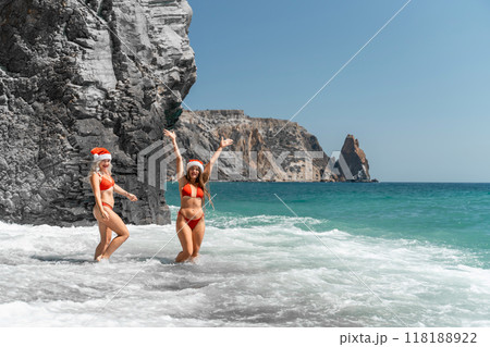 Women in Santa Claus hats run into the sea dressed in red swimsuits. Celebrating the New Year in a hot country Women in Santa Claus hats run into the sea dressed in red swimsuits. Celebrating the New Year in a hot country 118188922