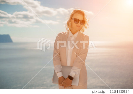 Freelance women sea working on a computer. Pretty middle aged woman with computer and phone outdoors with beautiful sea view. The concept of remote work. Freelance women sea working on a computer. Pretty middle aged woman with computer and phone outdoors with beautiful sea view. The concept of remote work. 118188934