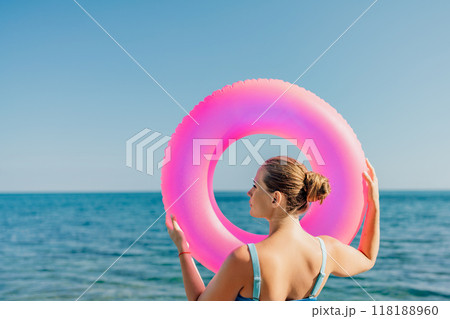 A woman is holding a pink inflatable ring in the ocean A woman is holding a pink inflatable ring in the ocean 118188960