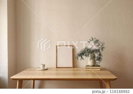 Warm Christmas Scandinavian interior. Minimal winter artistic composition. Blank vertical wooden picture frame mockup, cup of coffee on table. Pine tree branches, white vase. Beige wall background 118188982