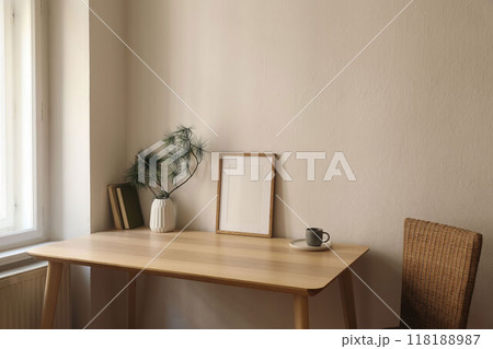 Cozy Christmas interior. Minimal winter home composition. Blank vertical wooden picture frame mockup, cup of coffee on table near window. Pine tree branches, white vase. Beige wall background 118188987