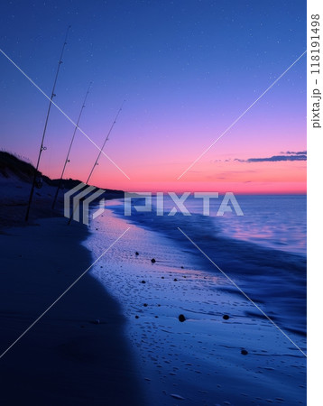 Twilight Fishing on Quiet Beach. Fishing rods stand on a quiet beach during twilight, with a tranquil sea and a beautiful pink and blue horizon at dusk. 118191498