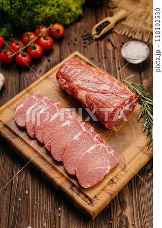 Raw pork loin with rosemary and fresh tomatoes on cutting board, perfect for culinary presentations 118192530