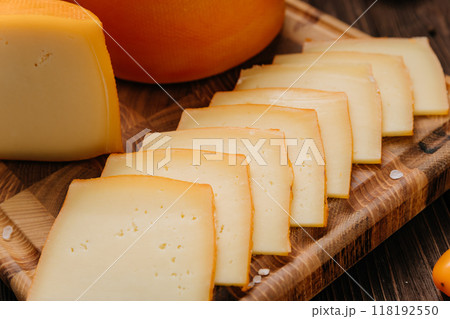 Wheel and slice of cheese on cutting board, perfect for culinary displays and gourmet presentations Wheel and slice of cheese on cutting board, perfect for culinary displays and gourmet presentations 118192550