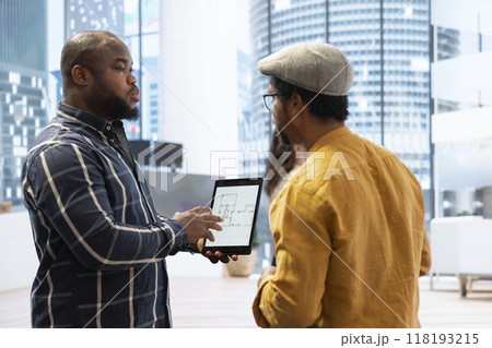 Real estate agent presenting a new office building to clients, discussing the detailed blueprints using a tablet during the property tour. Potential leasing investment opportunity. 118193215