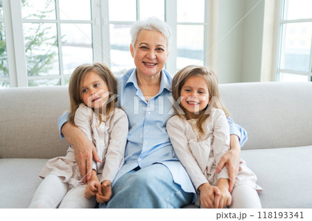 Happy family at home. Two little girls sisters twins grandmother enjoying time together. Good time at home. Grandma granddaughters child kids emotional bonding hugging together. Family generations 118193341